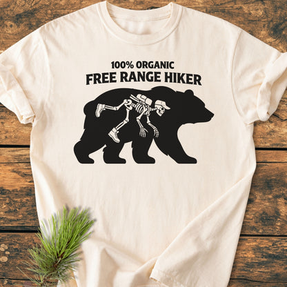 Organic Free Range Hiker - Vintage Wash Tee features a black bear silhouette with a skeleton hiker graphic, text above, laid on a wooden surface, showcasing its relaxed fit and garment-dyed softness.