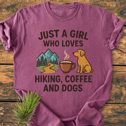 Just A Girl... Hiking Coffee Dogs - Vintage Wash Tee featuring a mountain, coffee mug, and dog icons, displayed on a wooden surface with a pine sprig, showcasing its relaxed, soft-washed fit.