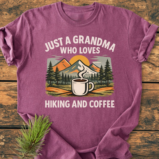 Grandma Loves Hiking And Coffee - Vintage Wash Tee: Maroon-purple T-shirt featuring a vibrant graphic of mountains, pine trees, and a coffee mug with text highlighting a love for hiking and coffee.