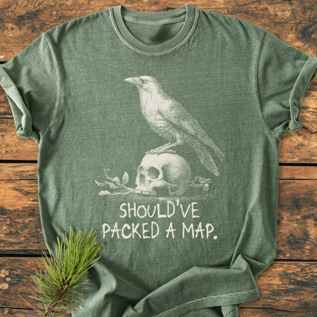 No WI-FI - Vintage Wash Tee features a crow perched on a skull with foliage, captioned “SHOULD’VE PACKED A MAP,” displayed on a rustic surface with a pine twig for styling.