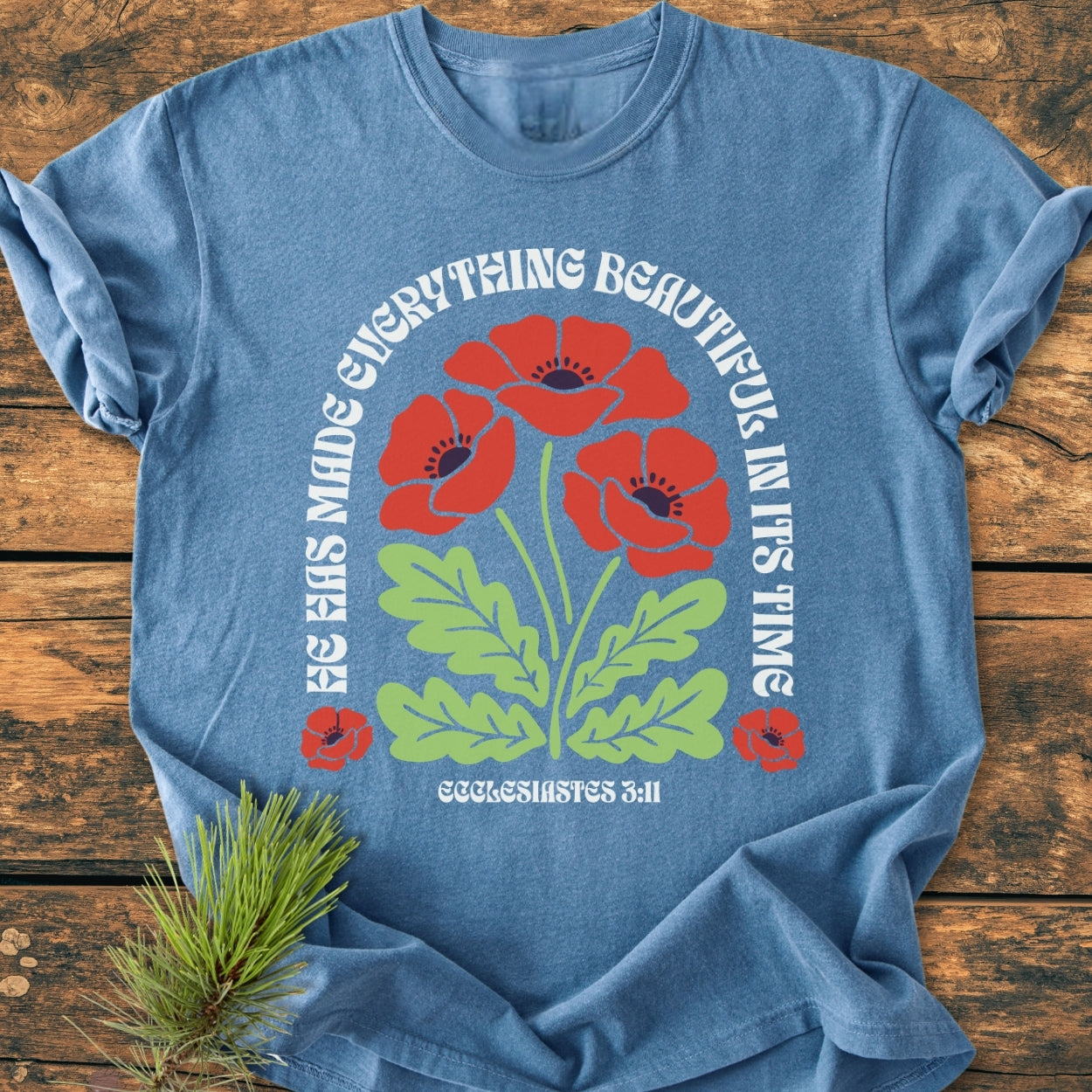 He Has Made Everything Beautiful - Vintage Wash Tee features three red poppies with green leaves and a Bible verse on a heather-blue Comfort Colors T-shirt, laid flat with a pine sprig beside.