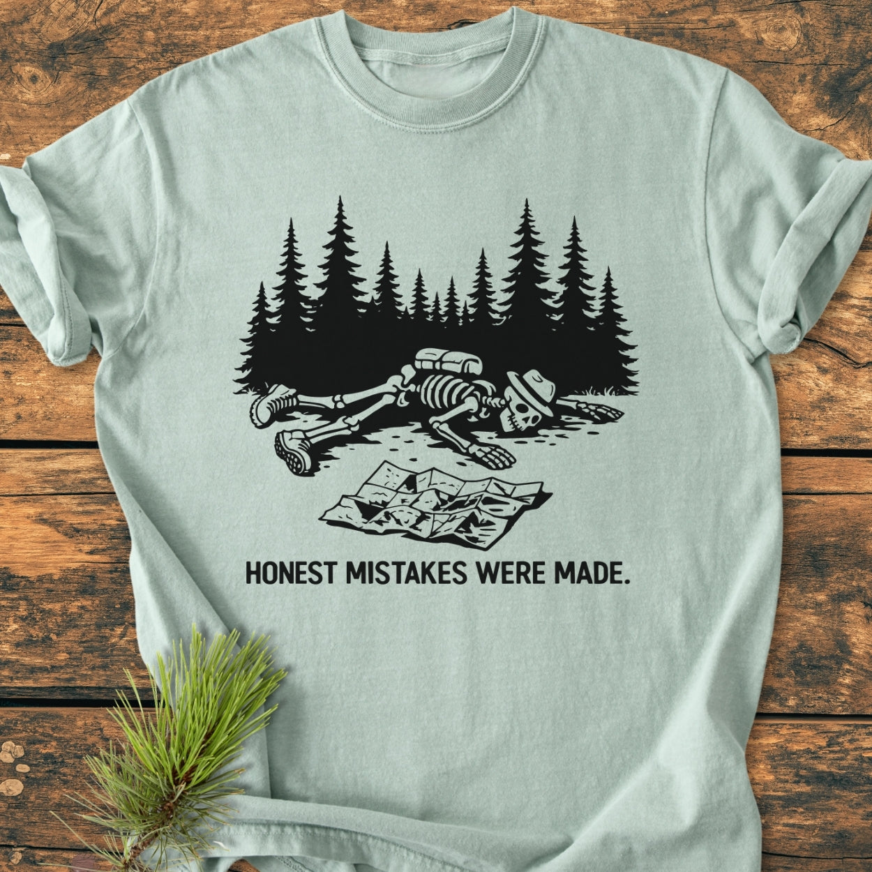 The Honest Mistakes Were Made - Vintage Wash Tee features a skeleton with hiking gear face-down, a crumpled map nearby, and the caption HONEST MISTAKES WERE MADE on soft, durable cotton.