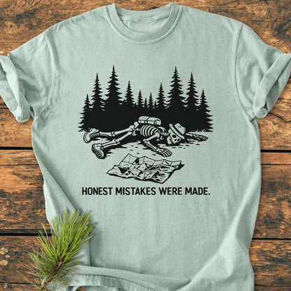 The Honest Mistakes Were Made - Vintage Wash Tee features a skeleton with hiking gear face-down, a crumpled map nearby, and the caption HONEST MISTAKES WERE MADE on soft, durable cotton.
