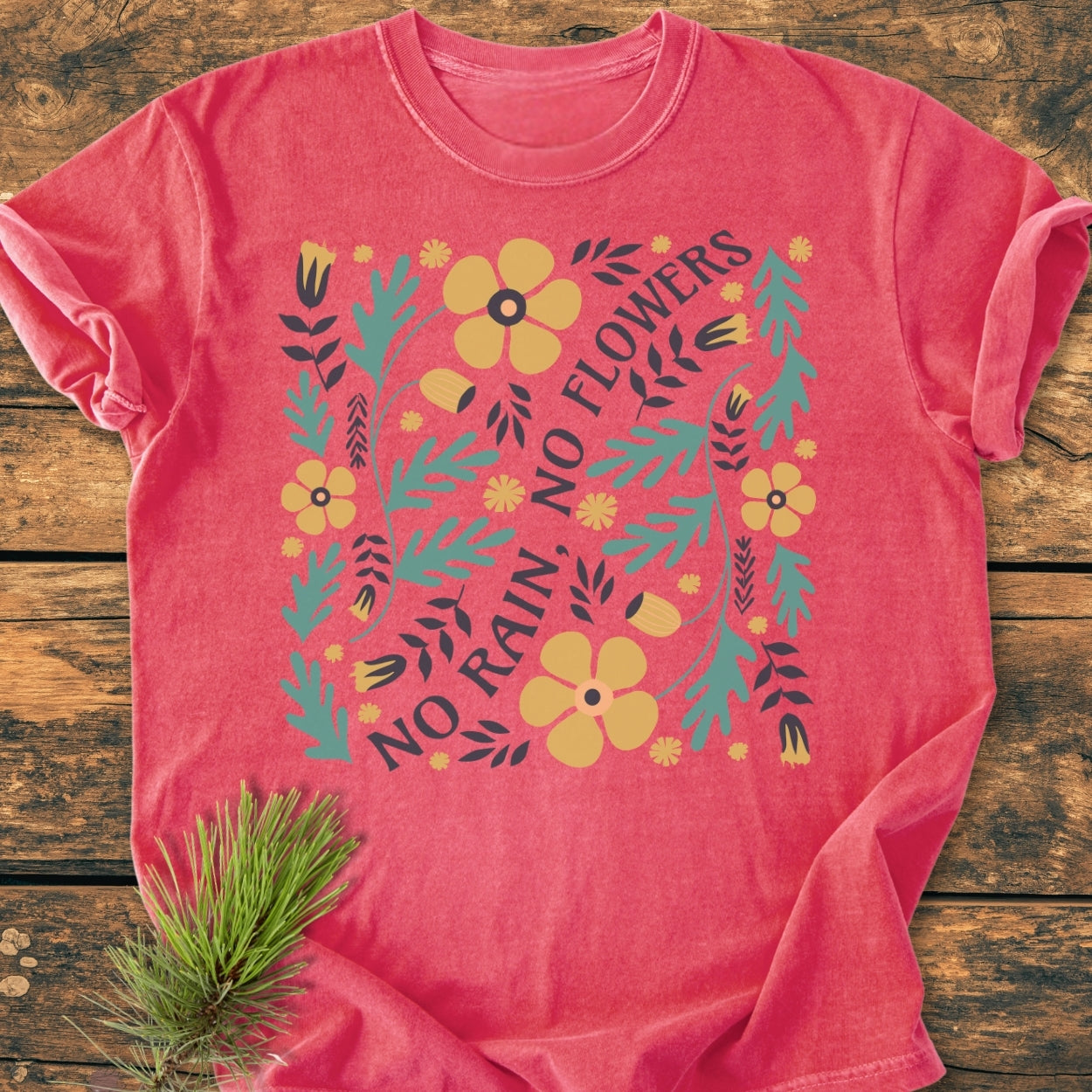 No Rain No Flowers - Vintage Wash Tee in heather-red, featuring a folk-style floral graphic with “NO RAIN, NO FLOWERS” text, laid on wood with pine sprig accent, emphasizing comfort and durability.
