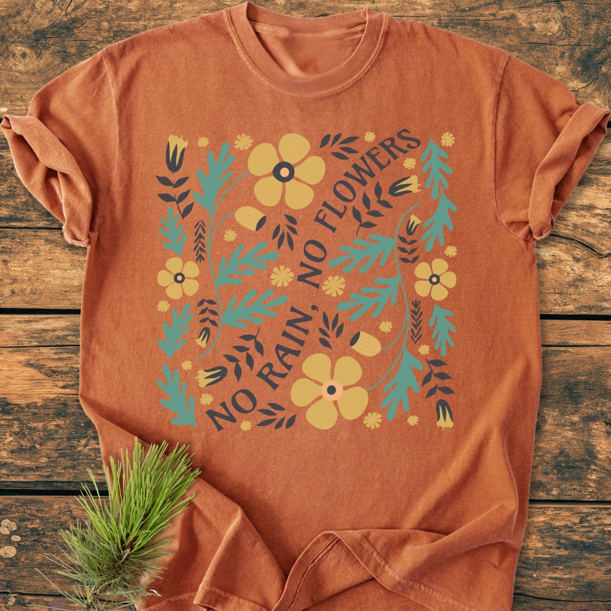 The No Rain No Flowers - Vintage Wash Tee features a floral design around the slogan, laid flat with a pine-branch accent. Crafted from soft, garment-dyed, 100% ring-spun cotton for durability.