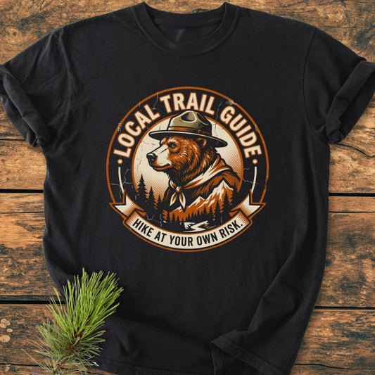 Local Trail Guide - Vintage Wash Tee featuring a circular logo with a bear in a ranger hat; laid on wood with pine, showcasing its relaxed fit and cozy, garment-dyed fabric.