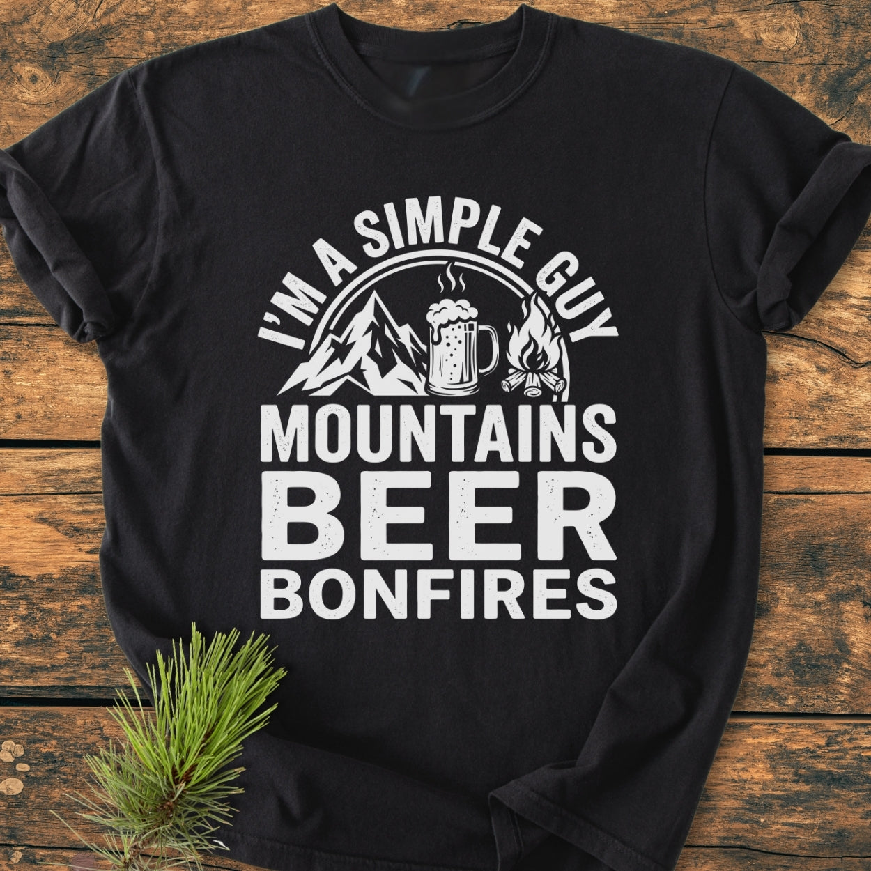 Mountains Beer Bonfires - Vintage Wash Tee on a wooden surface, featuring white text and icons. Made from soft, garment-dyed 100% ring-spun cotton, it offers a relaxed fit and durable double-needle stitching.
