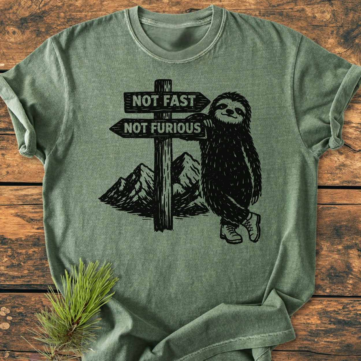 Not Fast Not Furious - Vintage Wash Tee features a stylized sloth in hiking boots leaning on a signpost with arrows reading “NOT FAST” and “NOT FURIOUS,” set against mountain silhouettes.