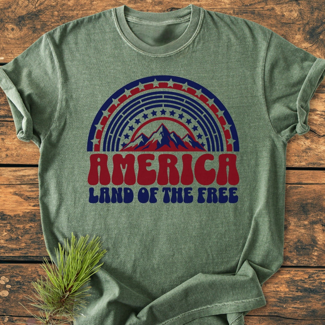 America Land Of The Free - Vintage Wash Tee with retro arch graphic and stars, laid on wood, accompanied by a pine sprig; crafted from soft, durable, relaxed-fit, garment-dyed 100% ring-spun cotton.
