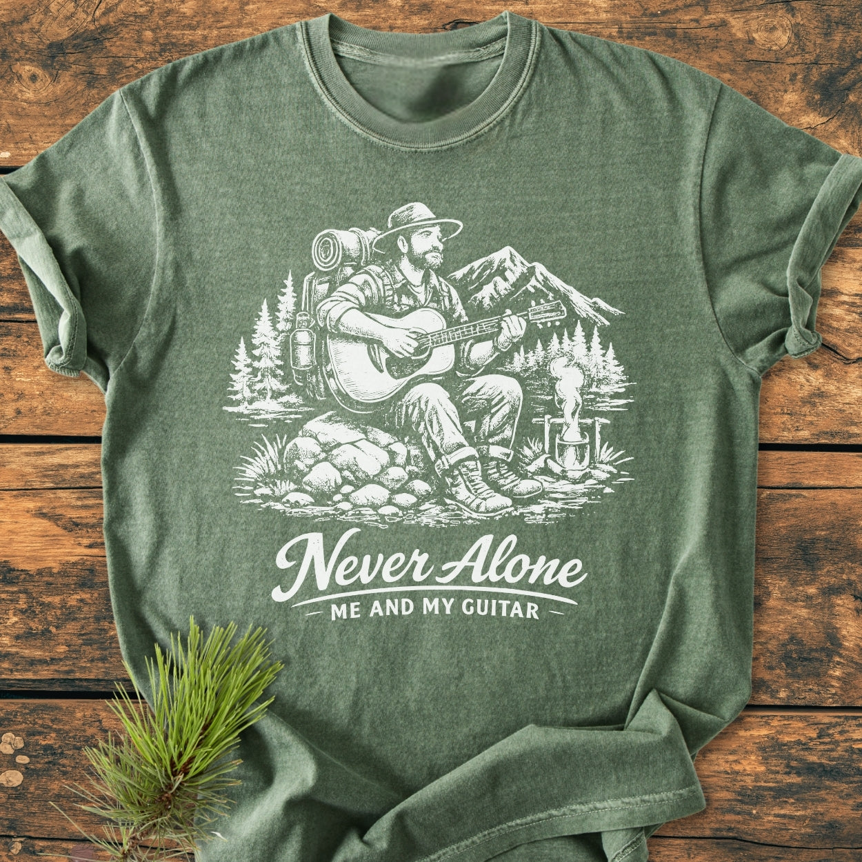 Never Alone. Me And My Guitar - Vintage Wash Tee features a detailed sketch of an outdoorsman with a guitar by a campfire, offering a cozy and durable fit with garment-dyed 100% cotton.