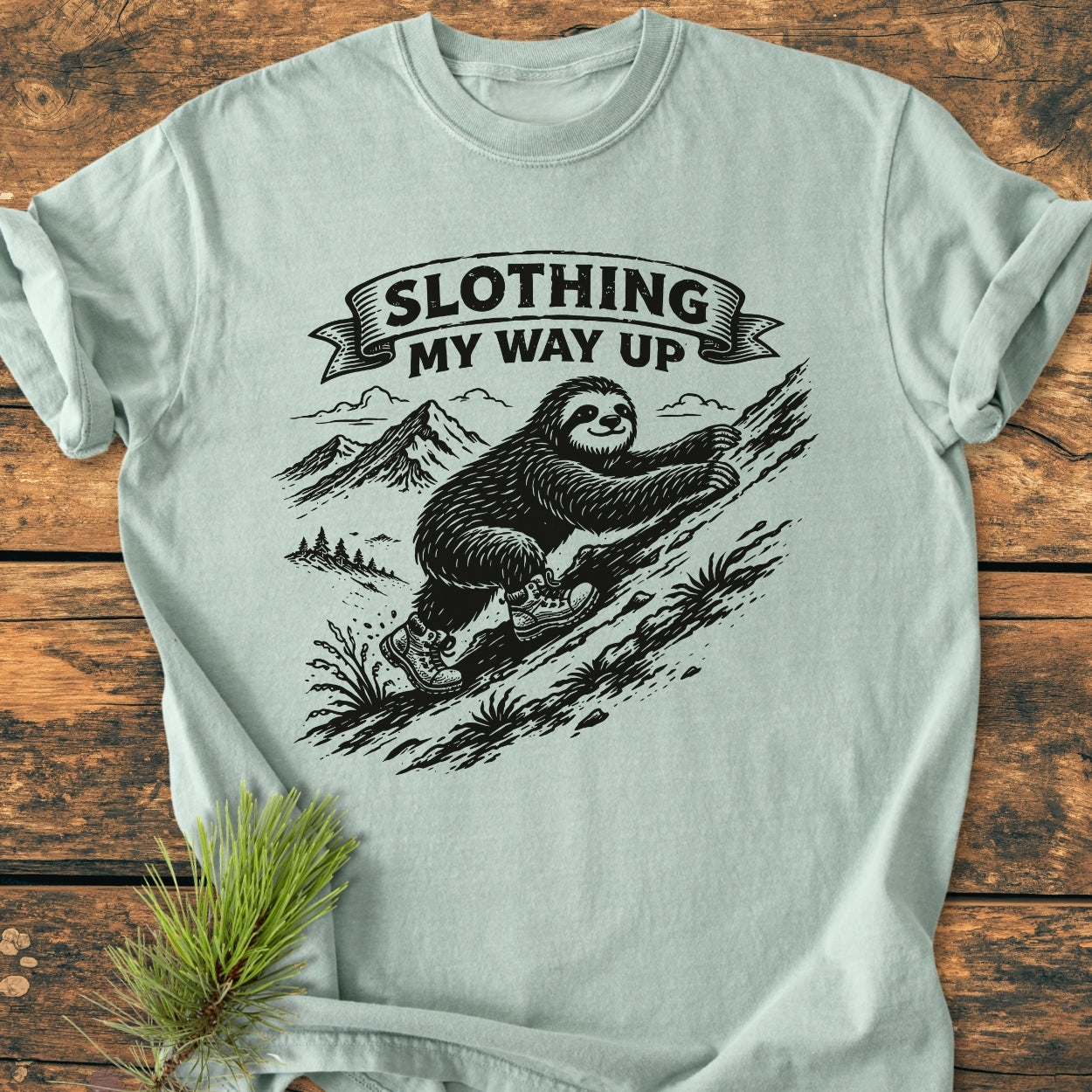 Slothing My Way Up - Vintage Wash Tee features a cartoon sloth in hiking boots on a mountainside. This Comfort Colors shirt offers a relaxed fit with durable, soft-washed 100% ring-spun cotton.