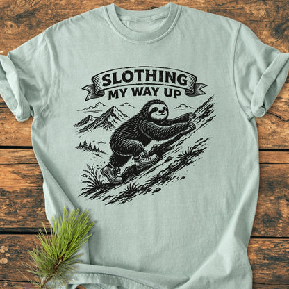 Slothing My Way Up - Vintage Wash Tee features a cartoon sloth in hiking boots on a mountainside. This Comfort Colors shirt offers a relaxed fit with durable, soft-washed 100% ring-spun cotton.
