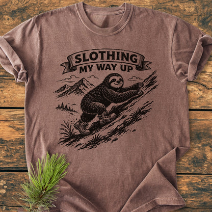 Slothing My Way Up - Vintage Wash Tee featuring a sloth illustration in hiking boots on a rocky hillside, laid on wood with a pine sprig. Soft, durable Comfort Colors fabric, perfect for everyday wear.