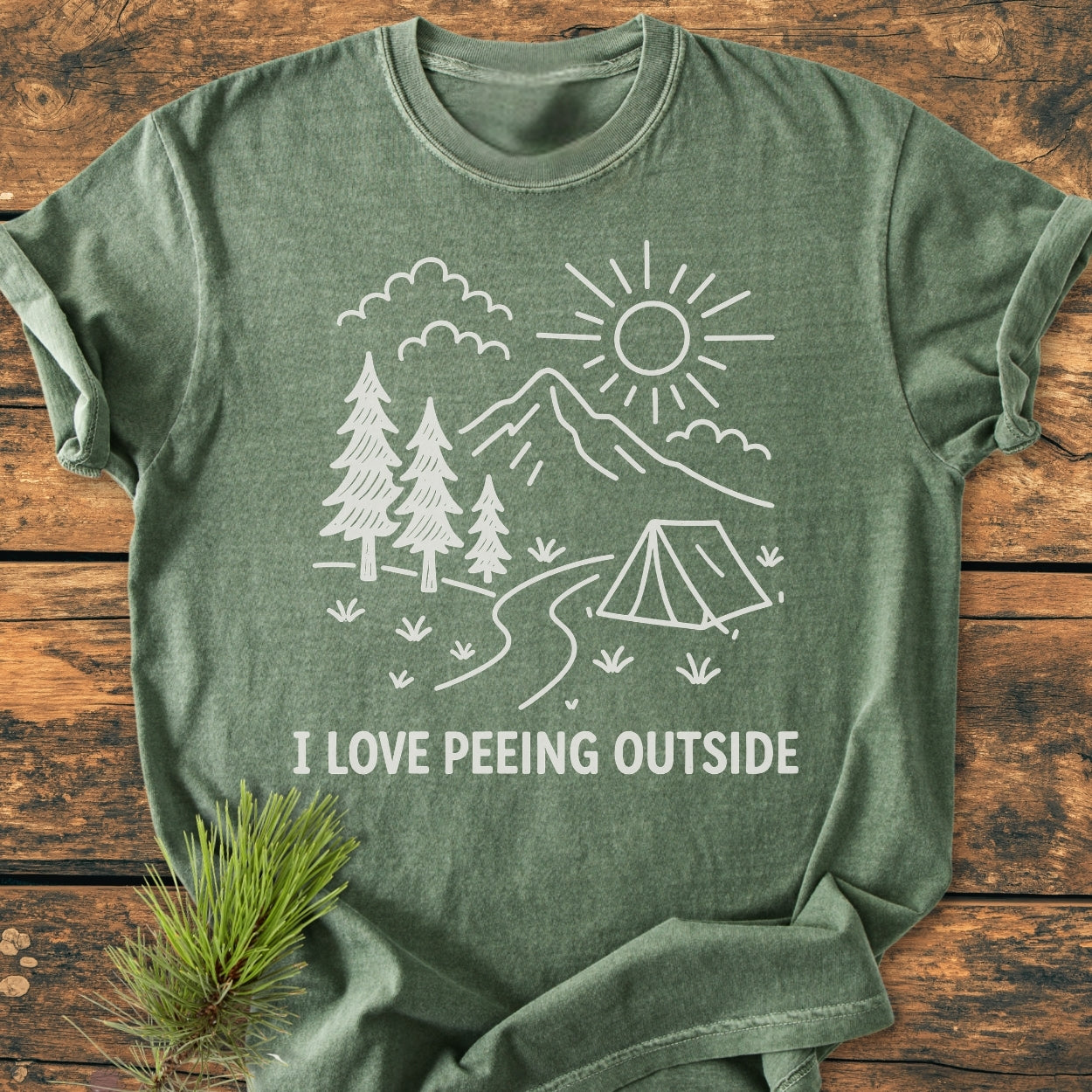 I Love Peeing Outside - Vintage Wash Tee features a hand-drawn illustration with pine trees, mountains, and a sun, printed on a forest-green, garment-dyed, relaxed fit Comfort Colors t-shirt.