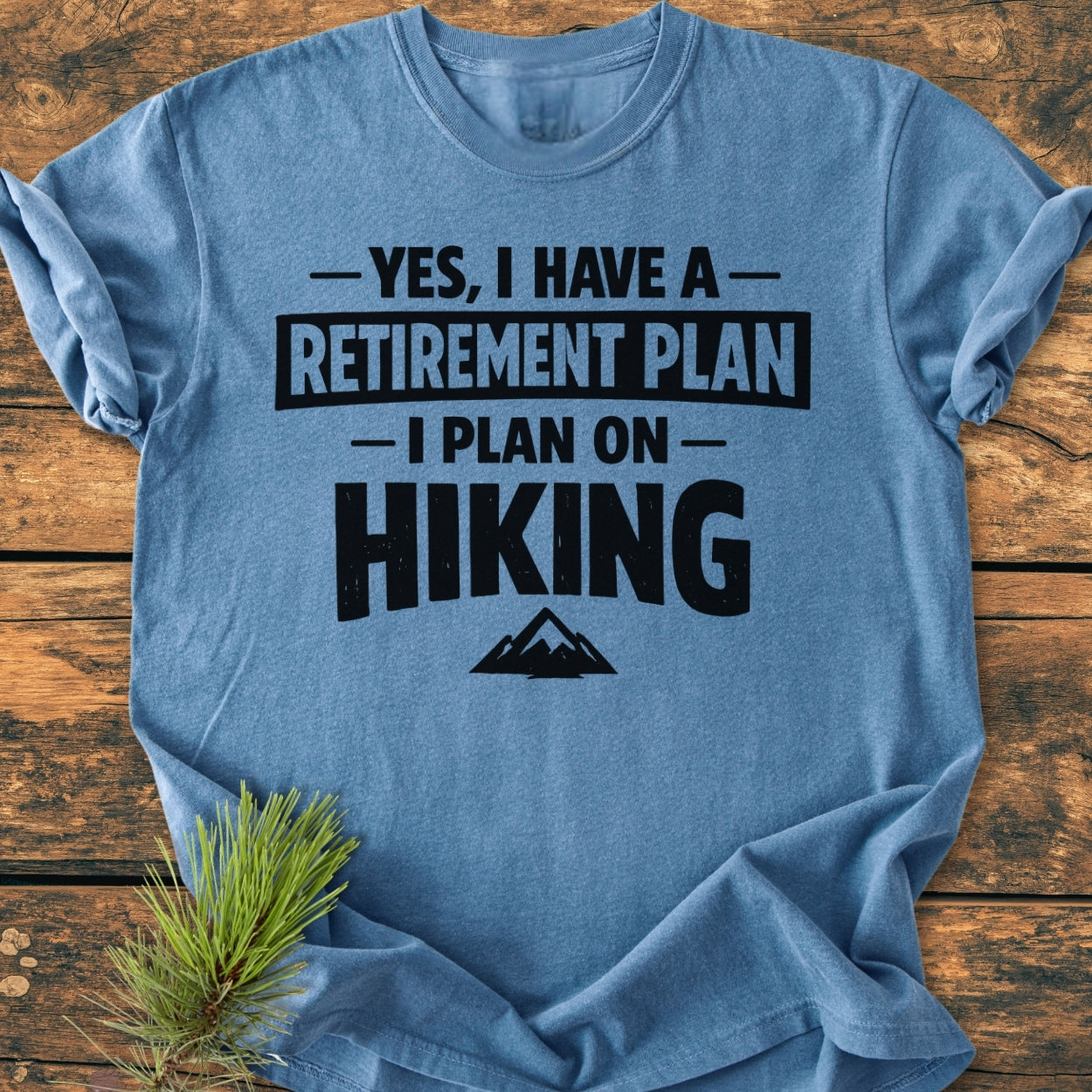 Retirement Plan Hiking - Vintage Wash Tee: Heather-blue, short-sleeve T-shirt with bold lettering and mountain graphic, laid on wood. Soft-washed, 100% ring-spun cotton, relaxed fit, durable stitching, ideal for cozy, casual wear.