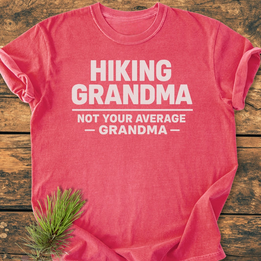 Hiking Grandma - Vintage Wash Tee with bold white slogan on salmon-pink fabric, laid flat. A pine sprig accents the soft, durable design, showcasing the tee's cozy, relaxed fit.