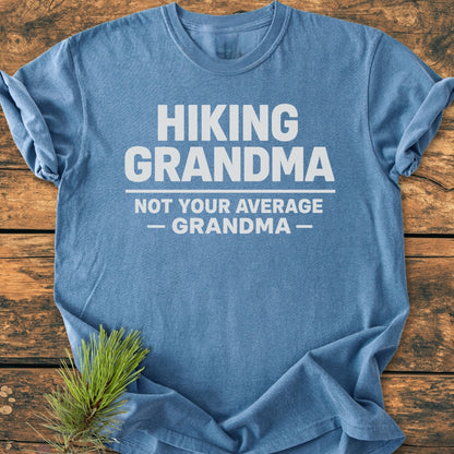 Hiking Grandma - Vintage Wash Tee: A heather-blue T-shirt with bold white slogan Hiking Grandma, Not Your Average — Grandma — printed on front, laid on wood with pine sprig accent.
