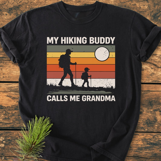 My Hiking Buddy Calls Me Grandma - Vintage Wash Tee features a retro sunset graphic with two hiking silhouettes, emphasizing its cozy, relaxed fit and durable, garment-dyed 100% ring-spun cotton fabric.