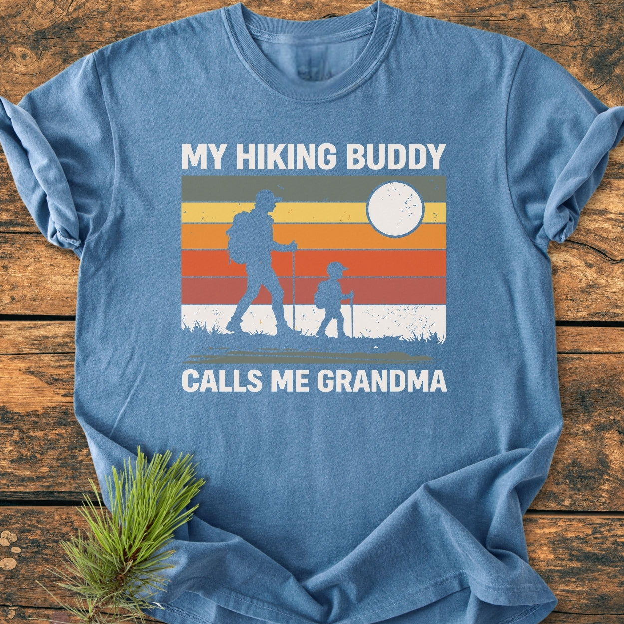 My Hiking Buddy Calls Me Grandma - Vintage Wash Tee: A heather-blue shirt featuring a sunset graphic with hikers, highlighting its soft, durable, garment-dyed cotton and relaxed fit for comfort.