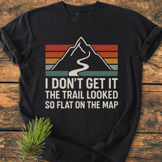 I Don't Get It - Vintage Wash Tee featuring a mountain graphic with retro stripes and a humorous slogan, laid on a wooden surface, beside a small pine sprig.