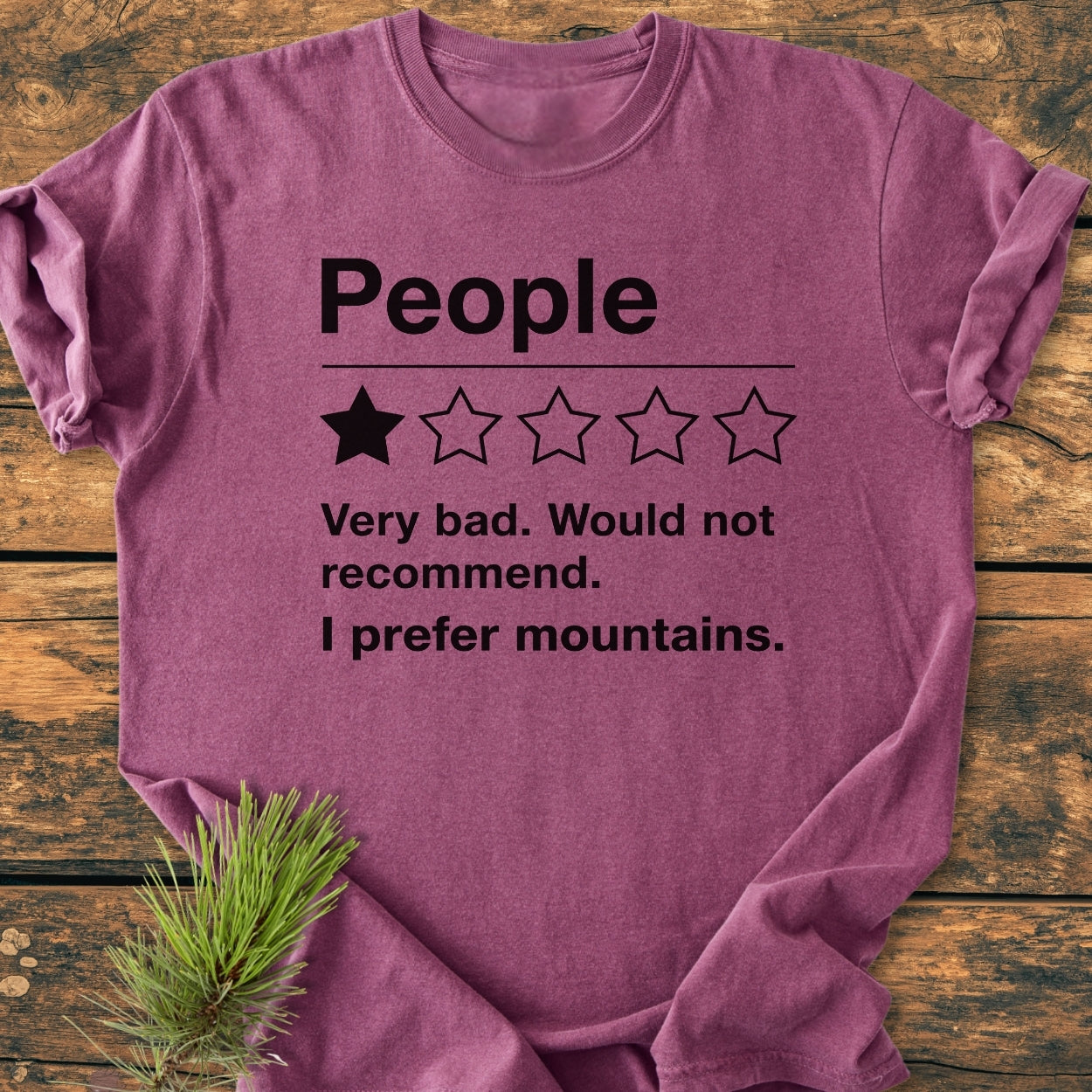 I Prefer Mountains - Vintage Wash Tee folded on wood, features a one-star “People” review print. Made of 100% soft-washed cotton, offering a relaxed fit and durable double-needle stitching.