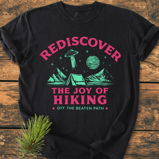 Rediscover The Joy Of Hiking - Vintage Wash Tee features a stylized mountain scene with an alien spacecraft, printed on a black T-shirt, emphasizing outdoor adventure and a relaxed fit.