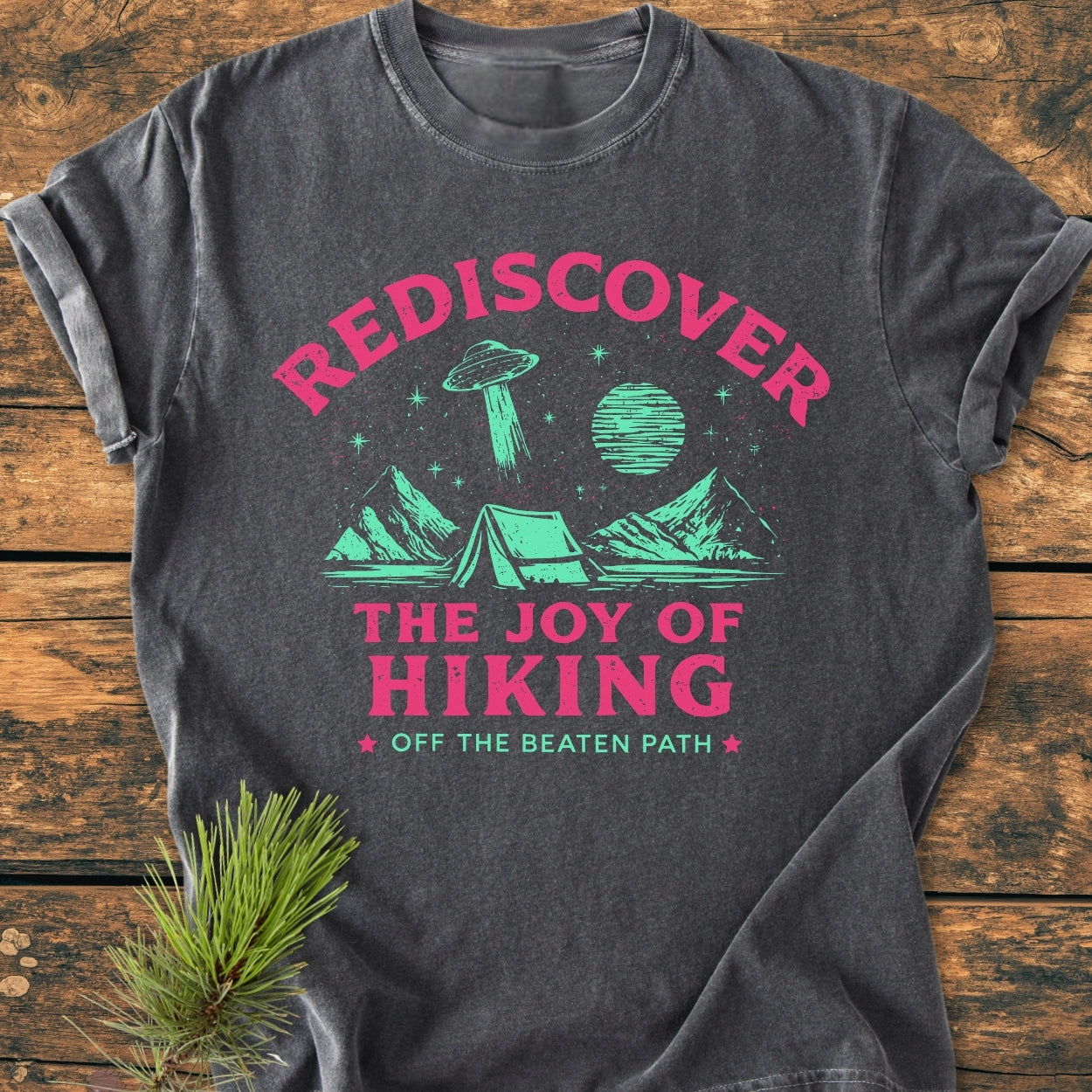 Rediscover The Joy Of Hiking - Vintage Wash Tee: Charcoal-gray T-shirt with a teal and magenta campsite graphic, rolled sleeves, laid on a wooden surface, highlighting a cozy, relaxed-fit, garment-dyed design.