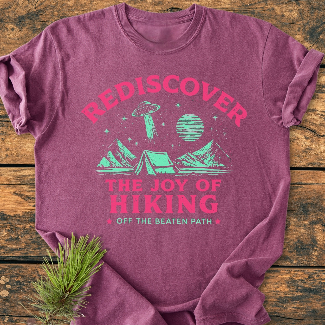 Rediscover The Joy Of Hiking - Vintage Wash Tee: Heathered magenta shirt with a stylized outdoor scene, featuring mountains, a tent, and UFO. Text reads “REDISCOVER THE JOY OF HIKING” and “OFF THE BEATEN PATH.”