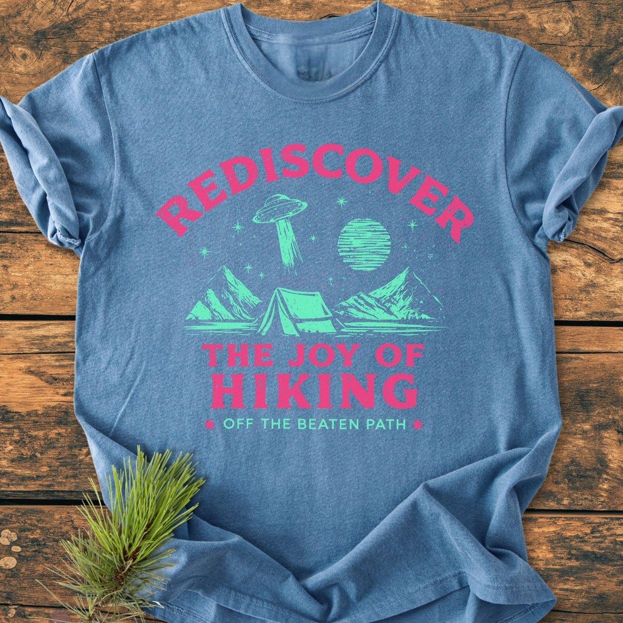 Rediscover The Joy Of Hiking - Vintage Wash Tee features a vibrant outdoor motif with mountains, tent, and UFO, screen-printed in mint green and pink on a soft blue, laid-flat garment.