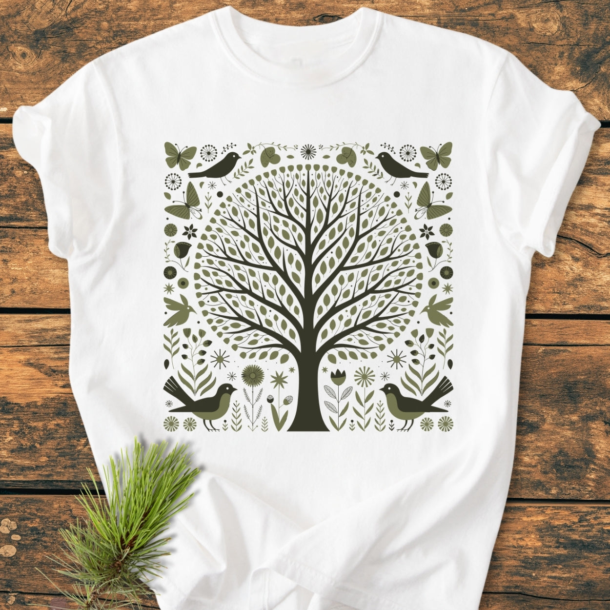 Nature Love - Vintage Wash Tee features a folk-art leafy tree design with birds and butterflies in olive and brown on a white, soft-washed, garment-dyed, 100% cotton T-shirt laid on wood.