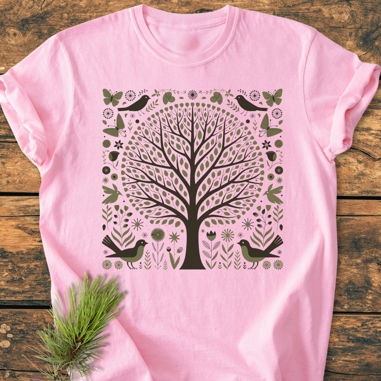 Nature Love - Vintage Wash Tee featuring a folk-art tree graphic with leaves, birds, and butterflies on a soft-pink surface, laid on wood. Made of soft-washed, garment-dyed 100% ring-spun cotton.