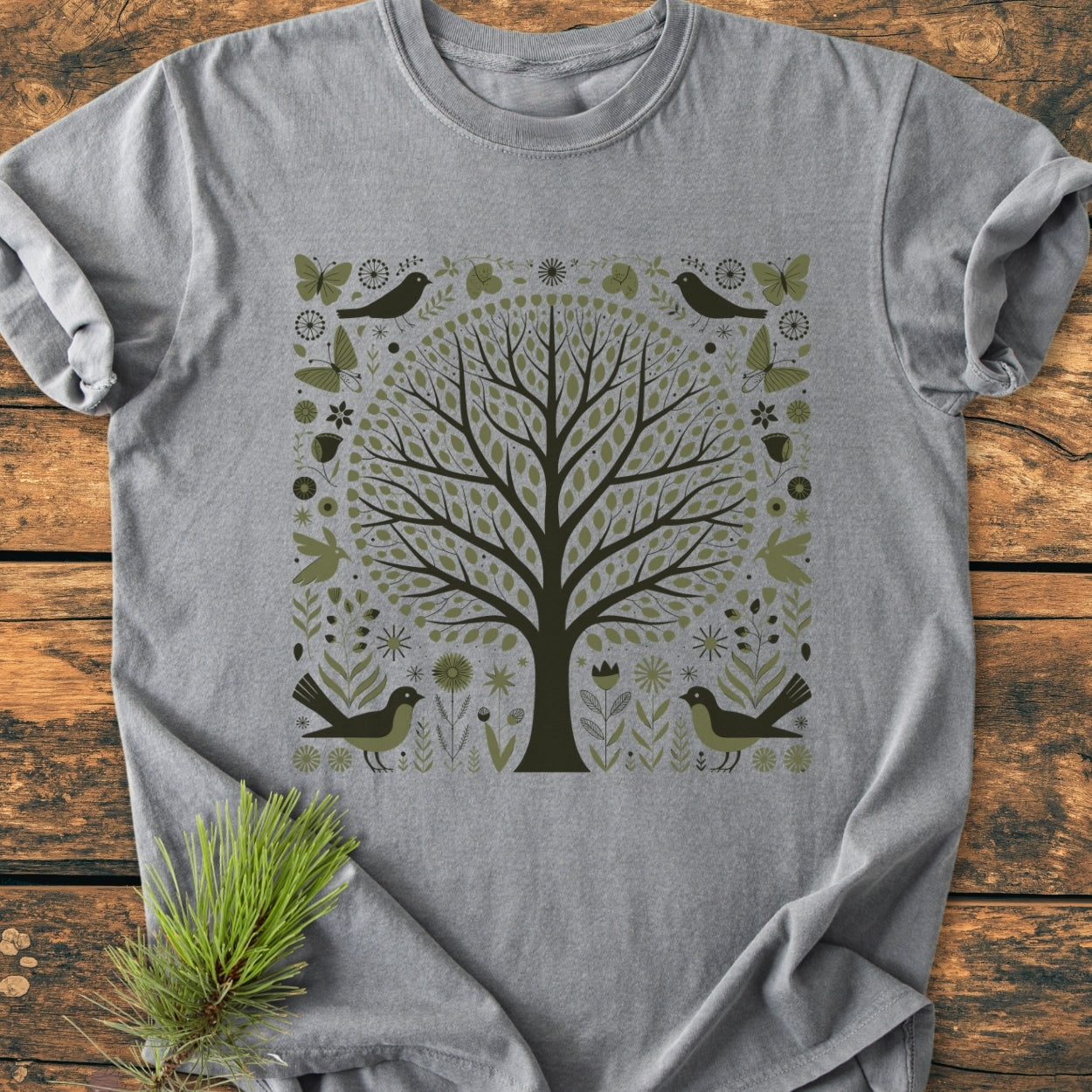 Nature Love - Vintage Wash Tee displayed on wood, features a stylized tree graphic with folk-art elements, emphasizing birds and butterflies. Made of soft-washed, pre-shrunk 100% ring-spun cotton, offering a relaxed fit.