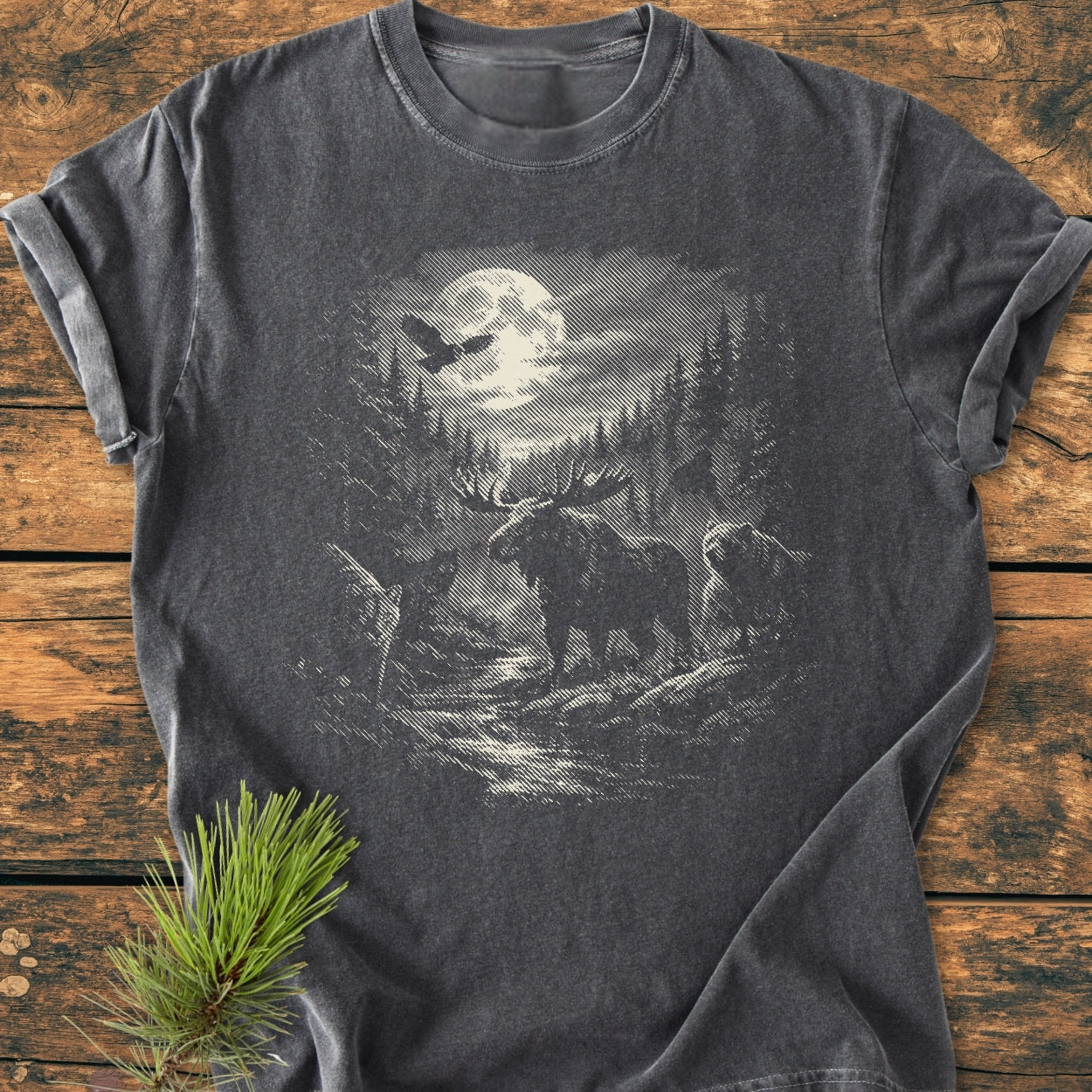 Moonlit Woodland - Vintage Wash Tee features an etched woodland scene with a moose, owl, bear, and forest stream on a dark-gray background, complemented by a pine sprig for a rustic touch.