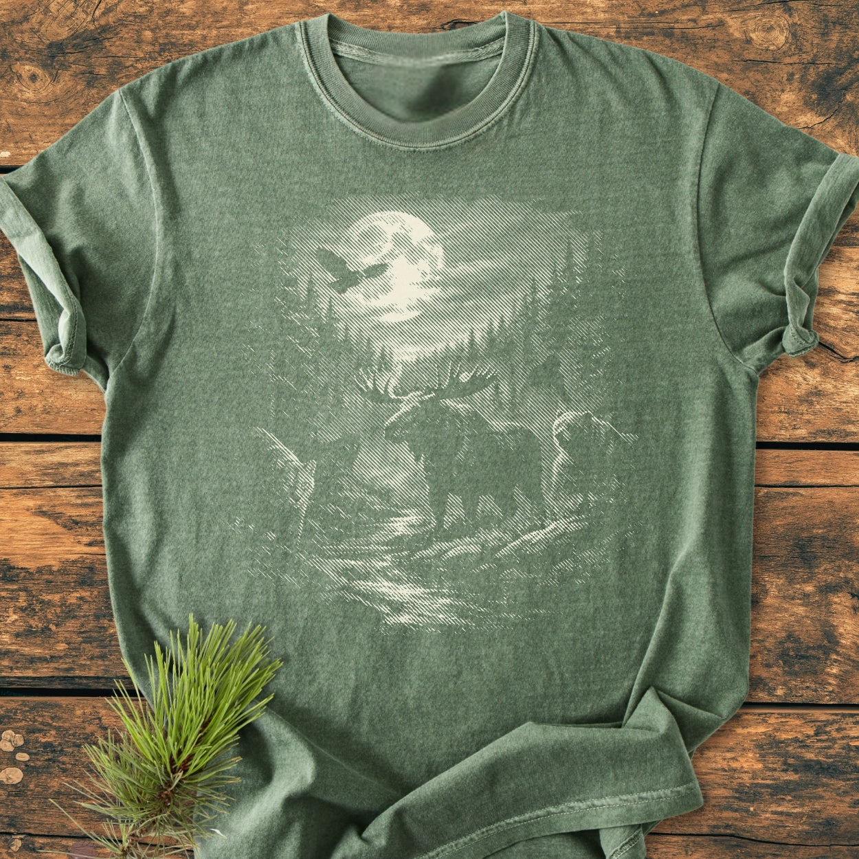Moonlit Woodland - Vintage Wash Tee features a heather-green T-shirt with a nature scene of a full moon, pine trees, an owl, elk, and bear, styled with a pine sprig accent.