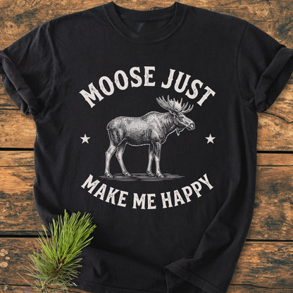 Moose Make Me Happy - Vintage Wash Tee featuring a hand-drawn moose and stars, laid flat on wood with a pine sprig. Relaxed fit, double-needle stitching, and 100% ring-spun cotton.