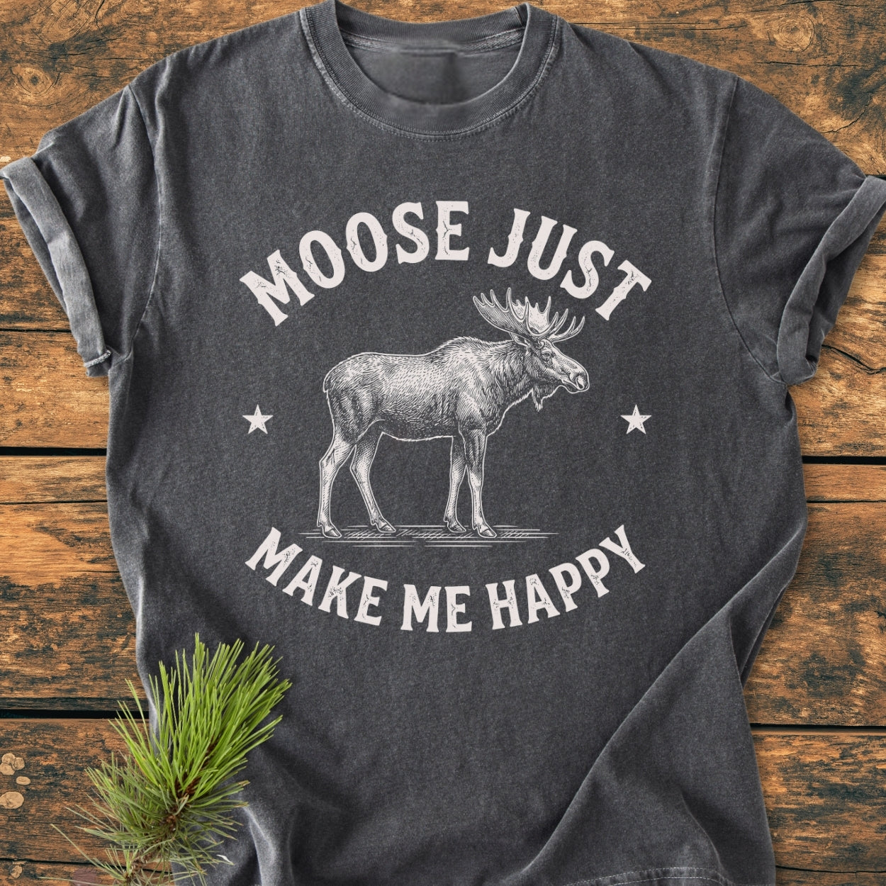 Moose Make Me Happy - Vintage Wash Tee features a white moose line-drawing with stars on a charcoal tee, sleeves rolled, laid flat on wood. Cozy, relaxed fit, crafted from 100% ring-spun cotton.