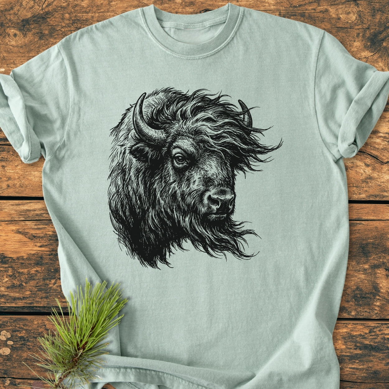 Silent Thunder - Vintage Wash Tee featuring a detailed black line-drawing of a bison's head, displayed on a wooden surface with a pine sprig beside it, highlighting its relaxed fit and durability.