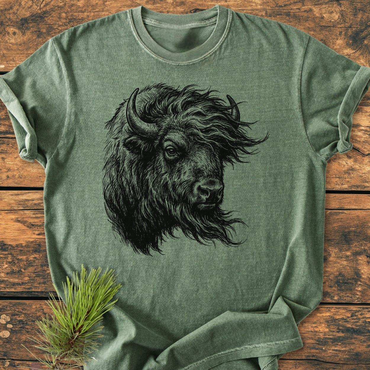 Silent Thunder - Vintage Wash Tee features a detailed bison head line-drawing on a heather-green fabric, laid flat with a pine branch beside it, embodying rustic charm and comfort.