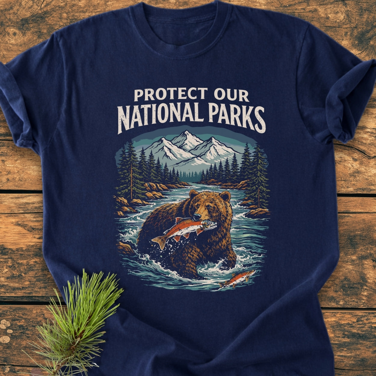 Protect Our National Parks - Vintage Wash Tee features a vibrant outdoor scene with mountains, trees, and a bear catching salmon, paired with a PROTECT OUR NATIONAL PARKS slogan on soft, durable cotton.
