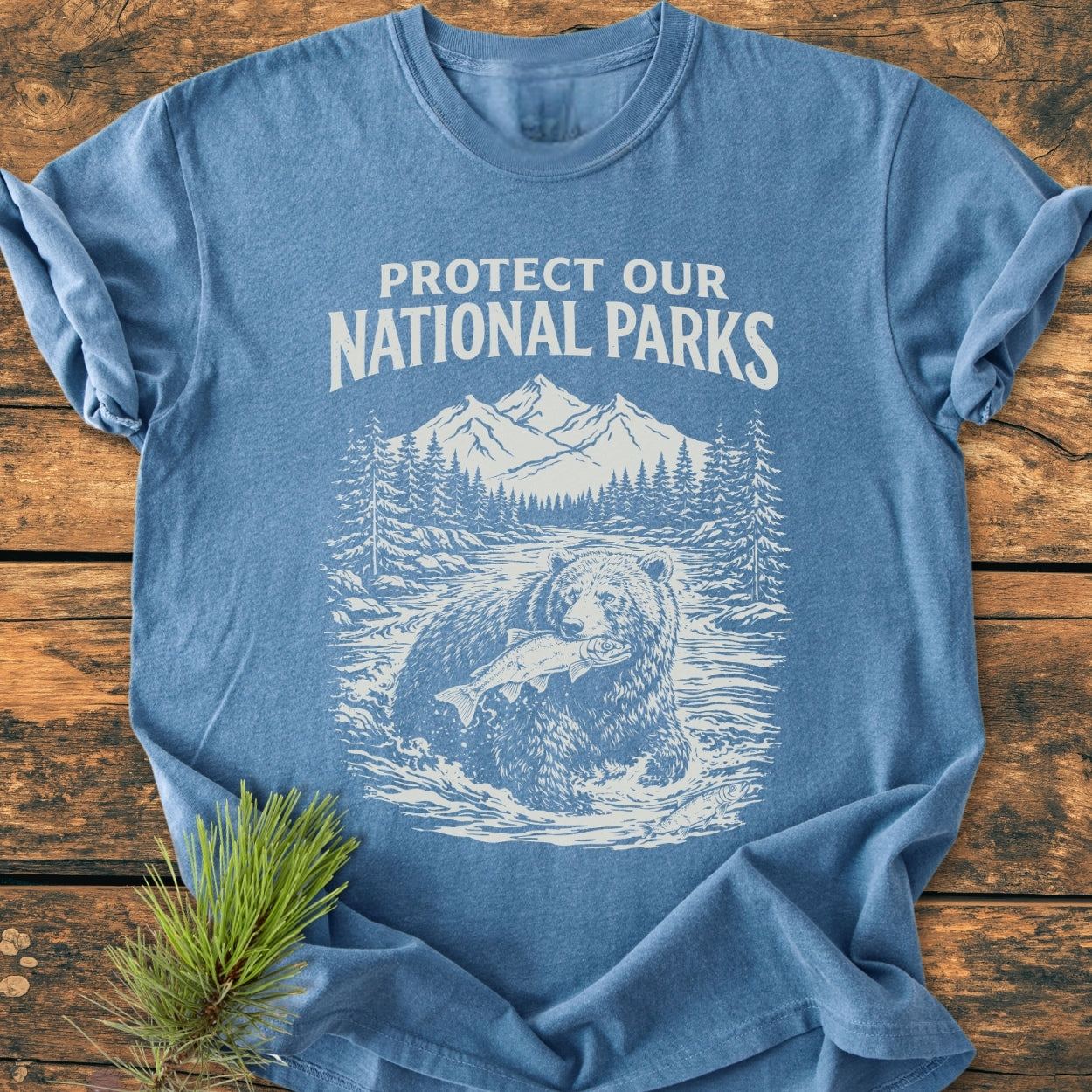 Protect Our National Parks - Vintage Wash Tee features a heather-blue design with an off-white print of a bear in a river scene. Crafted from soft, durable, pre-shrunk 100% ring-spun cotton.