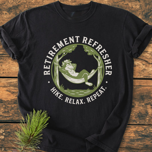 Retirement: Hike. Relax. Repeat - Vintage Wash Tee features a cartoon fox lounging in a hammock between trees, printed on a black T-shirt, with 'RETIREMENT REFRESHER' and 'HIKE. RELAX. REPEAT.' encircling.
