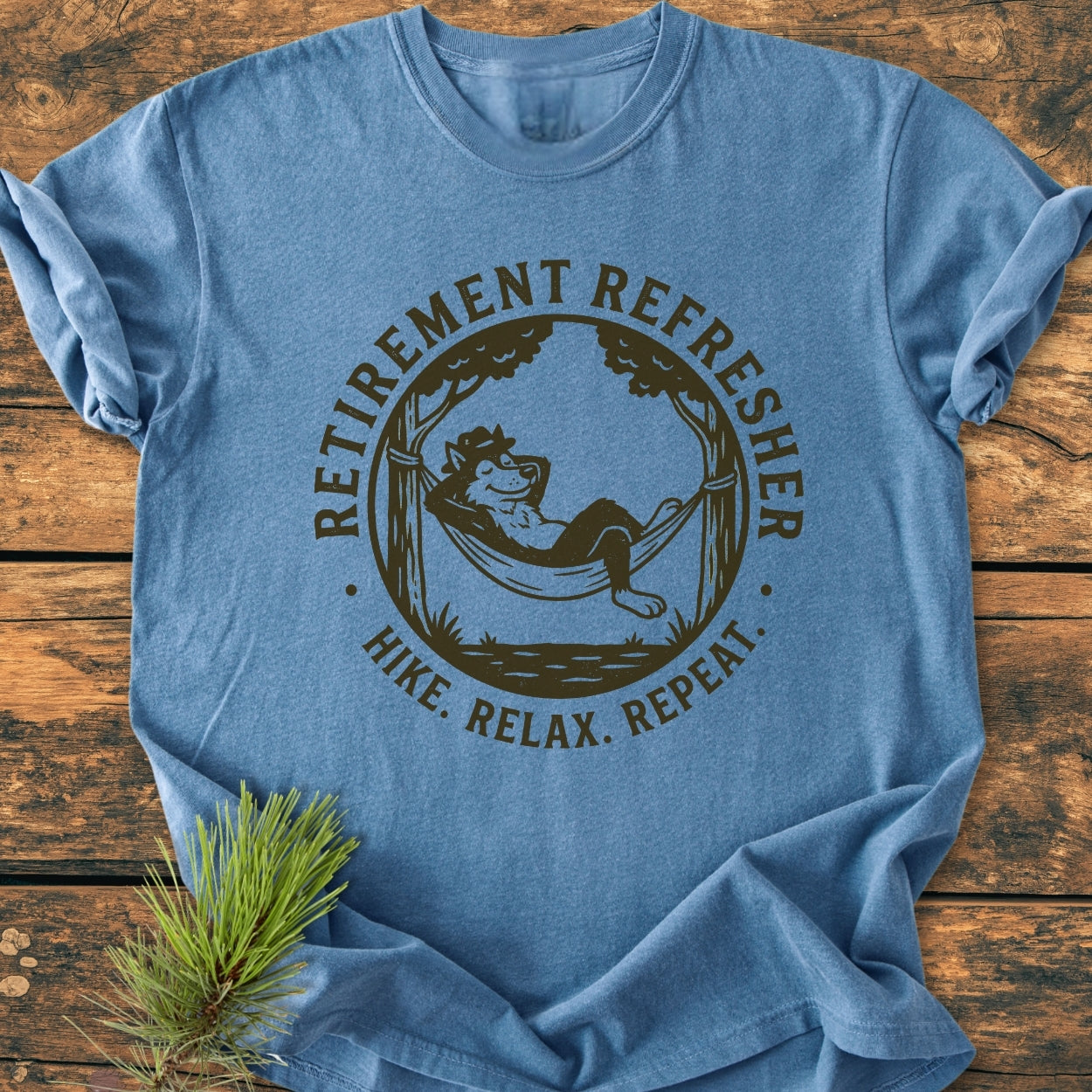 Retirement: Hike. Relax. Repeat - Vintage Wash Tee featuring a cartoonish wolf in a hammock between trees. The blue T-shirt is laid flat on wood with durable double-needle stitching and a relaxed fit.