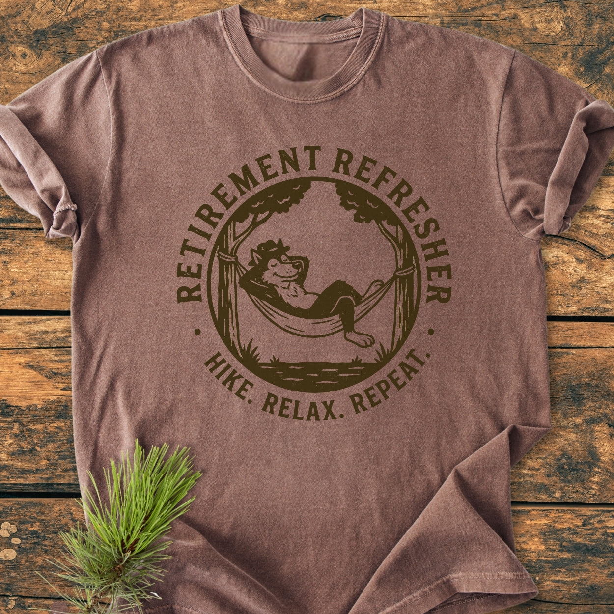 Heathered brown tee titled Retirement: Hike. Relax. Repeat - Vintage Wash Tee, featuring a circular design with a lounging animal in a hammock, enhancing the shirt's cozy, rustic appeal.
