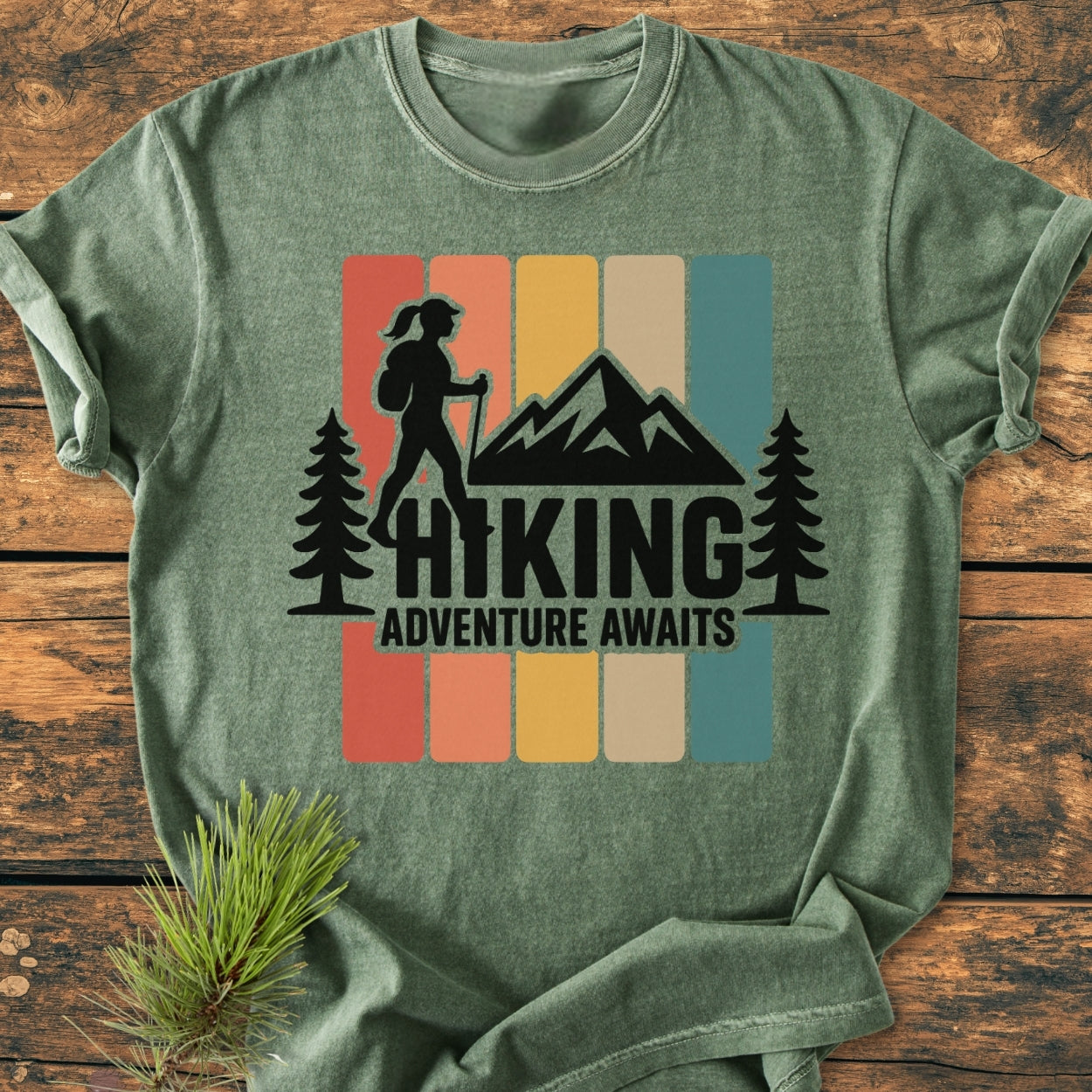 Hiking Girl - Vintage Wash Tee: Heather-green T-shirt featuring a stylized outdoor scene with a mountain, pine trees, and a hiker silhouette, complemented by HIKING and ADVENTURE AWAITS text.