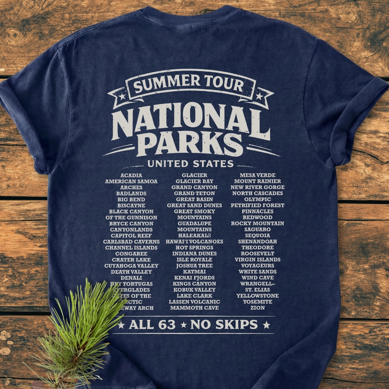 Summer Tour National Parks BACK PRINT - Vintage Wash Tee, featuring a vintage-style graphic listing all 63 U.S. National Parks, laid on wood with a pine sprig, showcasing its relaxed fit and durability.