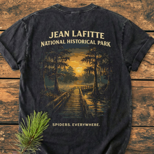Back of Spiders. Everywhere. BACK PRINT - Vintage Wash Tee, featuring a swampy boardwalk illustration with cypress trees and text “JEAN LAFITTE – NATIONAL HISTORICAL PARK.” Laid on wood with pine sprig accent.