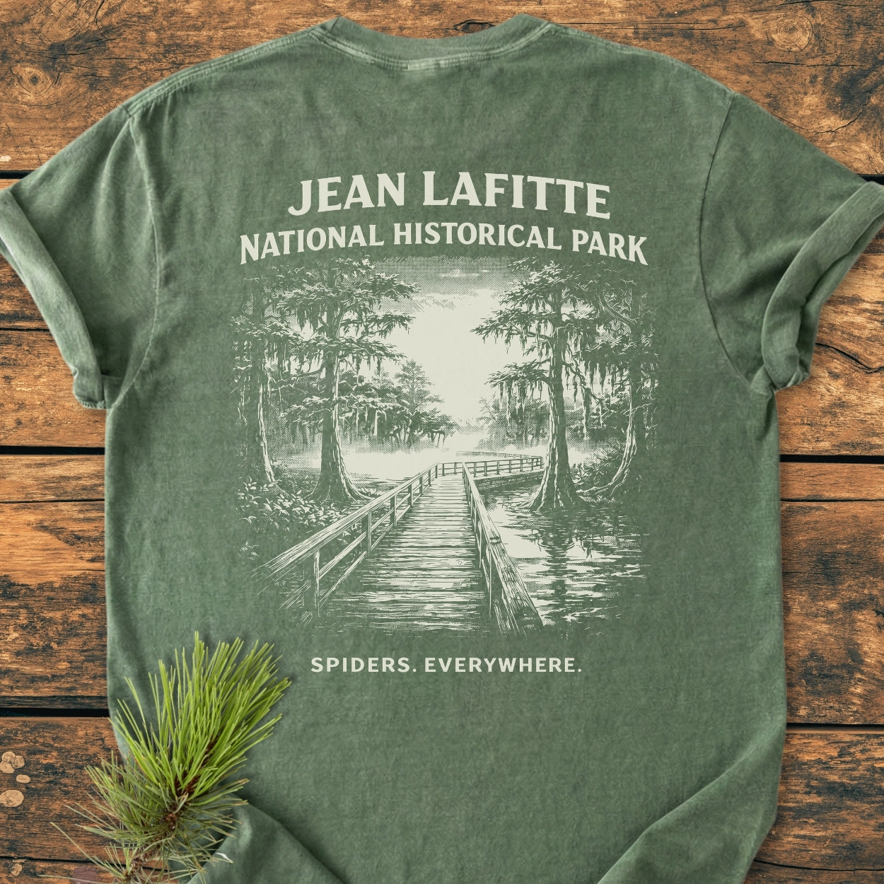 Spiders. Everywhere. BACK PRINT - Vintage Wash Tee featuring a boardwalk and cypress swamp scene. Short-sleeved, laid on wood, with pine sprig accent, crafted from soft, durable, ring-spun cotton.