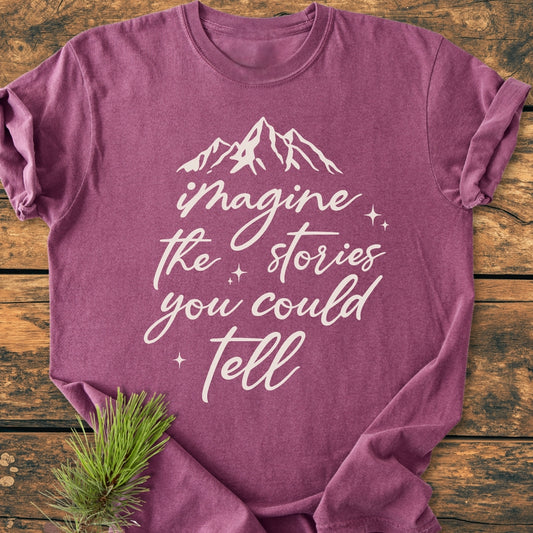 Imagine The Stories - Vintage Wash Tee with white script and mountain silhouette, laid on wood. Features a cozy, relaxed fit, pre-shrunk ring-spun cotton, showcasing durability with double-needle stitching.
