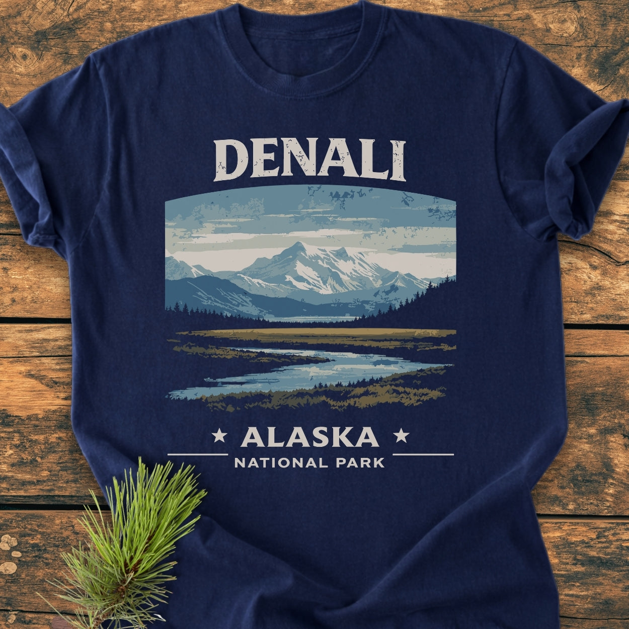 Denali National Park - Vintage Wash Tee featuring a rugged mountain landscape print, laid on wood with a pine sprig. Soft, garment-dyed, 100% cotton, relaxed fit, ideal for everyday wear.