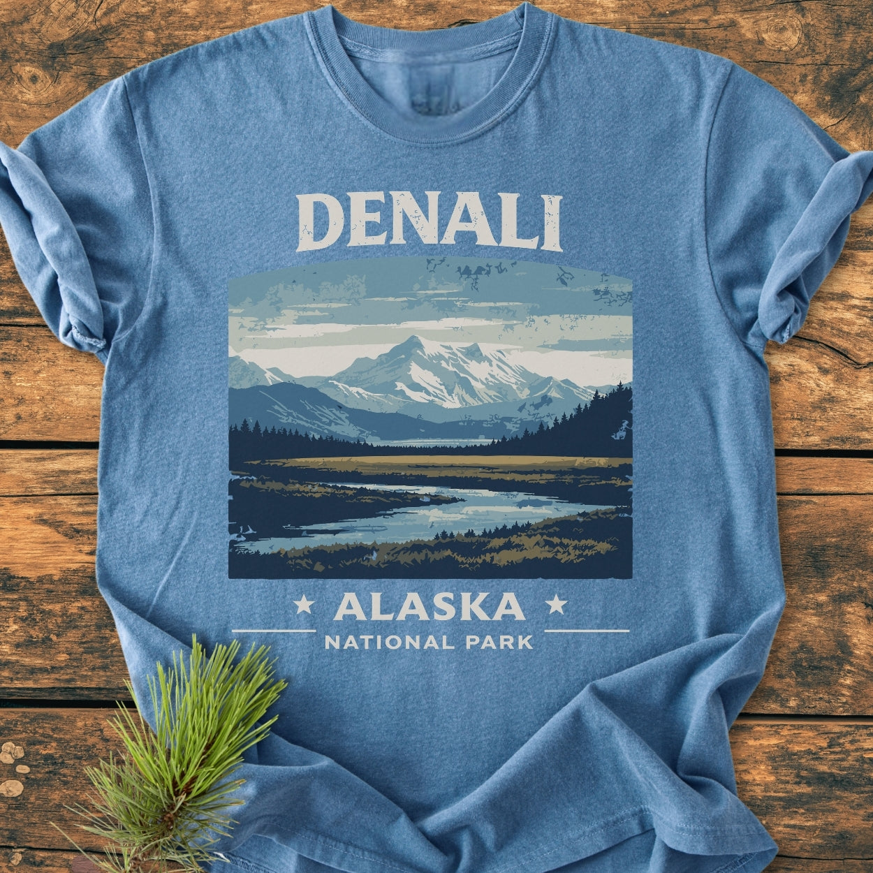 Denali National Park - Vintage Wash Tee features a graphic of Denali with forest, river, and DENALI ALASKA NATIONAL PARK. A spruce sprig accents the soft, garment-dyed, relaxed-fit T-shirt.
